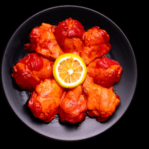Alitas adobadas crudas sobre plato negro, listas para cocinar.