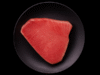 Filete crudo de atún importado sobre plato negro y fondo negro, presentación premium.