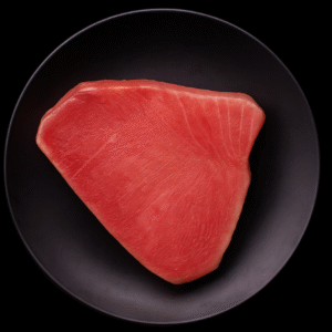 Filete crudo de atún importado sobre plato negro y fondo negro, presentación premium.