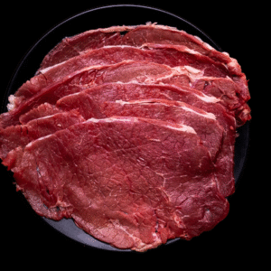 Bistec Selecto crudos de res finamente rebanados servidos en un plato negro sobre fondo negro.