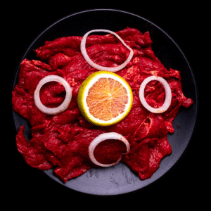 Tiras de carne marinada enchilada cruda, marinadas con chile rojo y decoradas con aros de cebolla y naranja sobre plato negro.