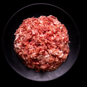 Carne molida de res cruda servida en un plato negro sobre fondo negro.