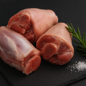 Codillo de cerdo crudo sobre fondo negro con sal de grano y romero fresco