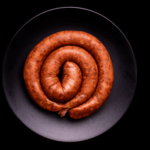 Longaniza selecta cruda en forma de espiral, colocada sobre un plato negro con fondo oscuro tipo estudio fotográfico.
