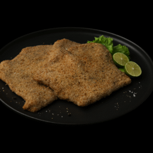 Dos piezas de milanesa de res empanizadas servidas en un plato negro, acompañadas de rodajas de limón y lechuga sobre fondo oscuro.
