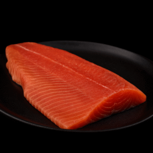 Lonja de salmón crudo sobre plato negro, vista lateral.